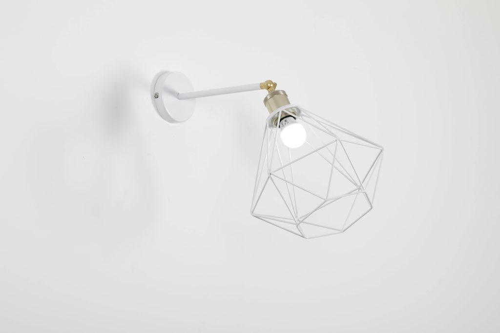 A contemporary wall-mounted lamp with a geometric cage design against a white wall.