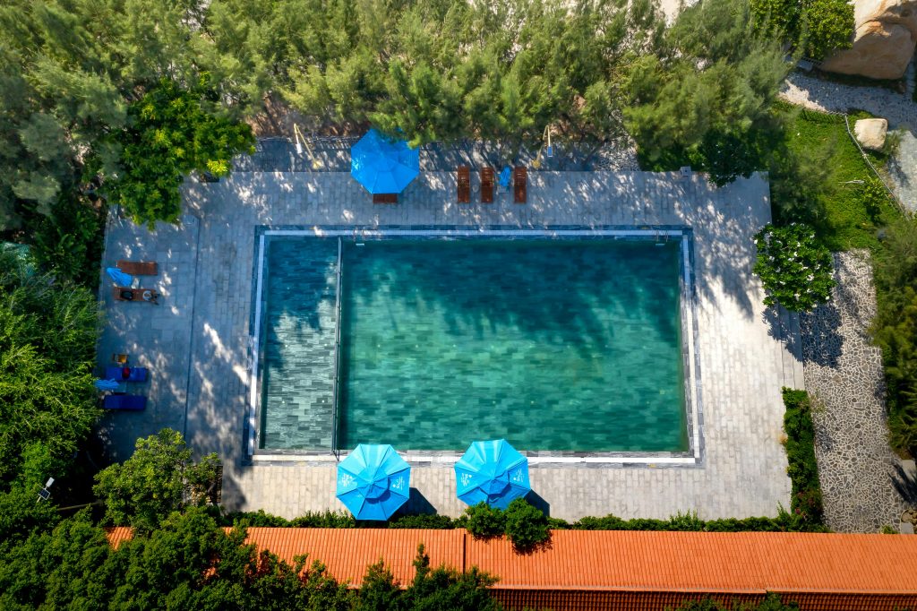 A tranquil bird's-eye view of a secluded swimming pool surrounded by lush greenery and blue umbrellas.