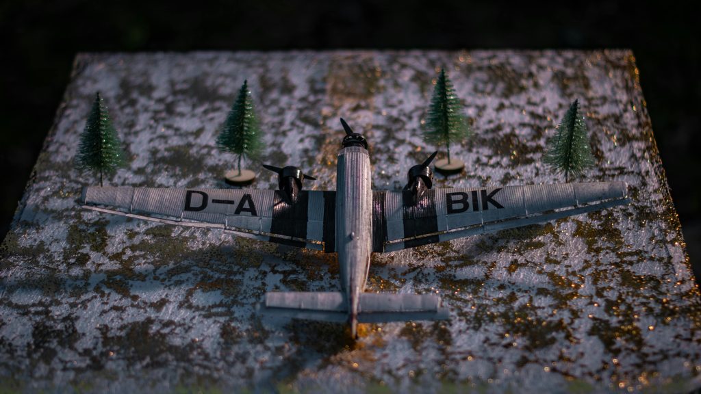 Close-up of a miniature airplane model surrounded by tiny trees on a textured, snowy surface.