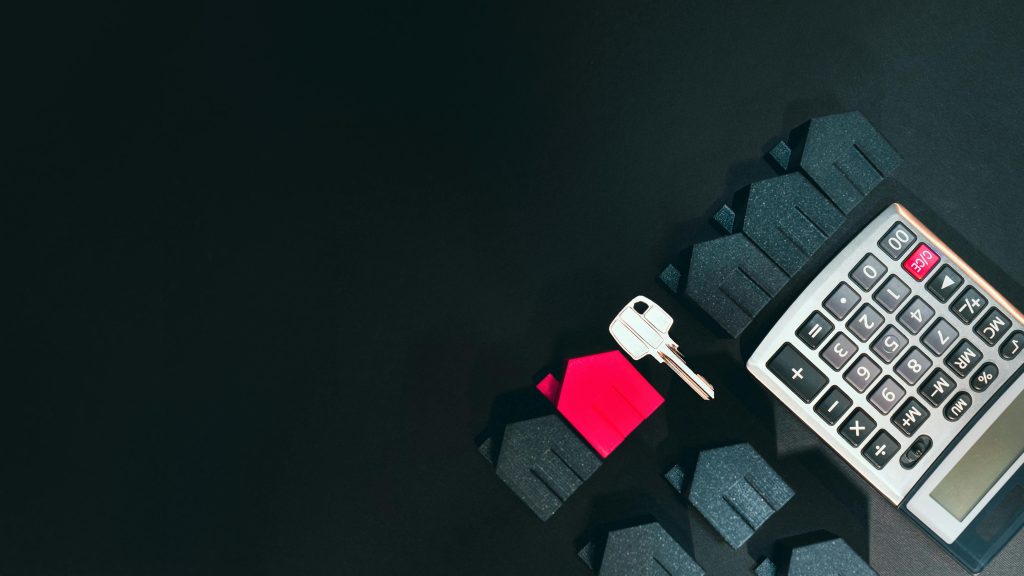 Real estate concept image featuring a calculator, houses, and a key on a black background.