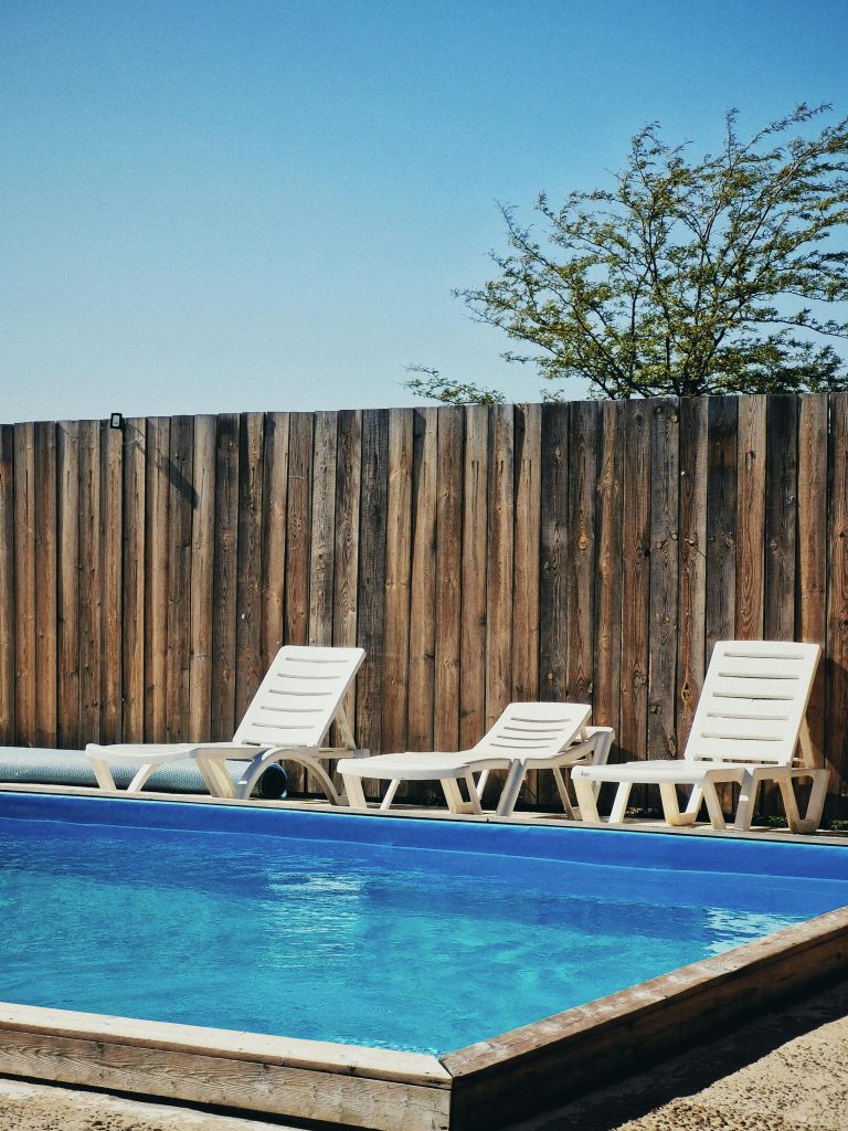 Relax by the serene poolside with chairs and wooden fence on a sunny day.