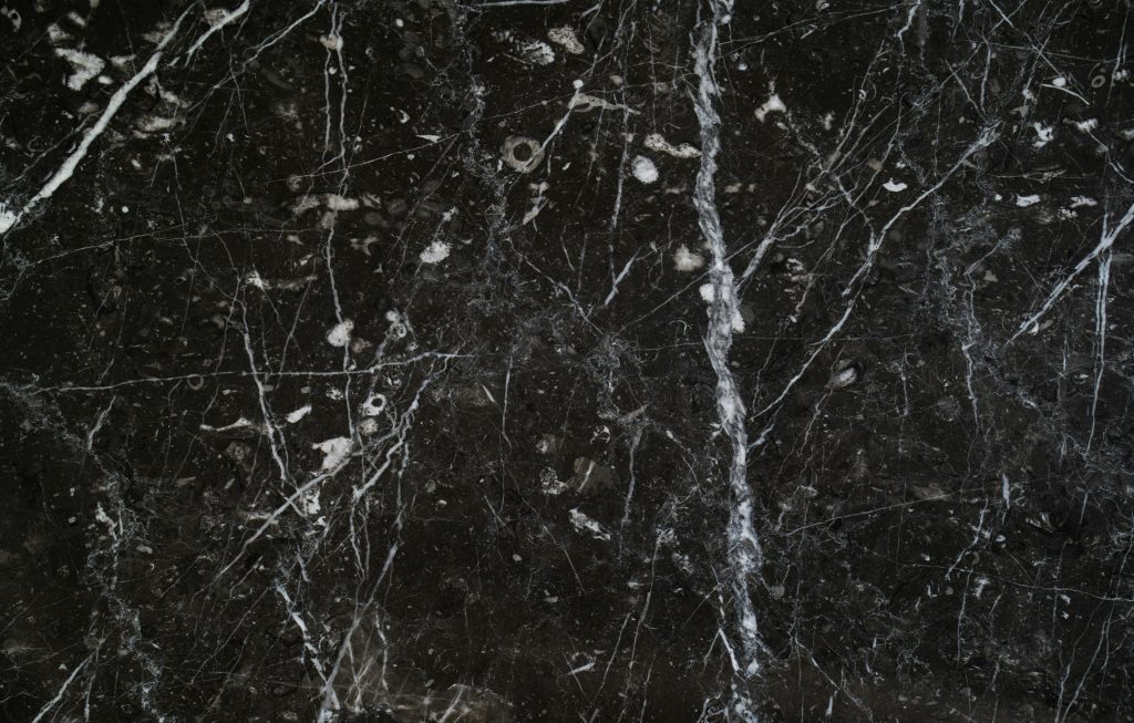 Close-up view of cracked black marble surface with intricate white veins, creating a natural pattern.