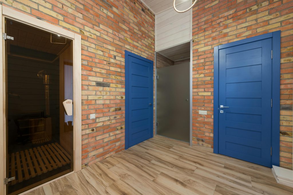 A stylish interior featuring blue doors, brick walls, and a sauna room in a cozy home setting.