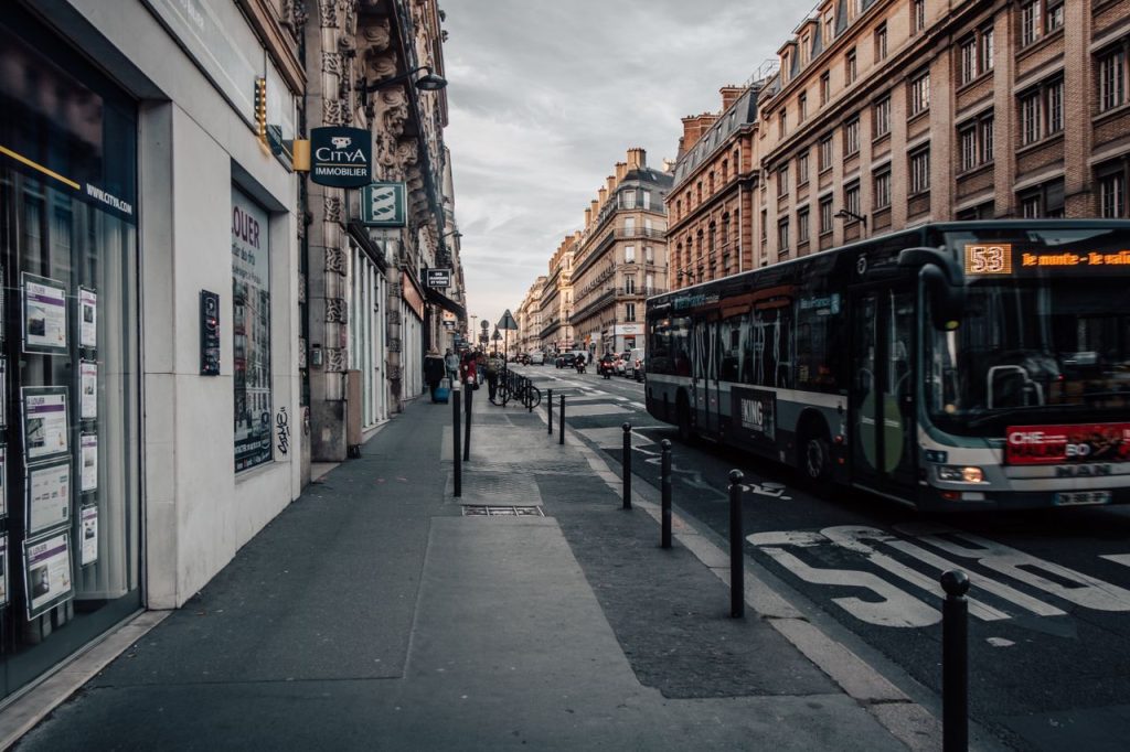 A bustling Paris street scene with a bus, historic buildings, and a quiet sidewalk atmosphere.